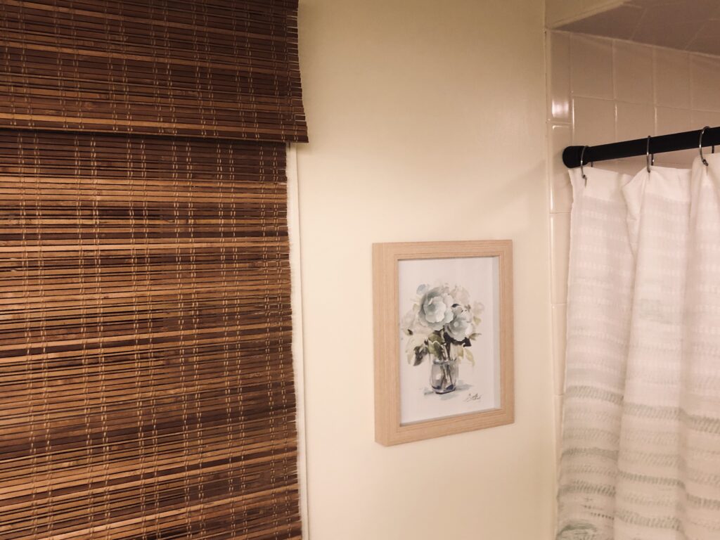 Bathroom Details featuring a bamboo textured window shade, cream colored walls, a handmade floral wall art, and green ombre shower curtain
