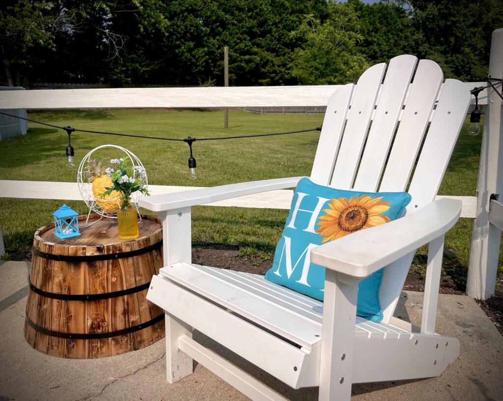 Patio Vignette of White Adirondack Chair with teal throw pillow and barrel side table with summertime decor